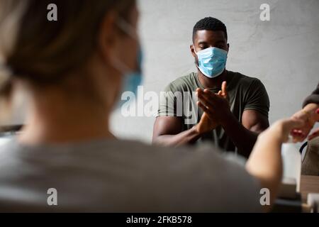 Donna imprenditore che applica sanitizer mentre collega maschio che siede vicino a. ufficio durante la pandemia Foto Stock