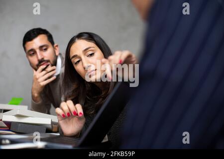 Imprenditori maschili e femminili che discutono sopra il laptop in ufficio Foto Stock