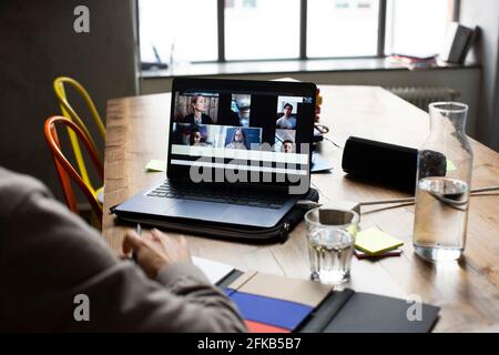 Mano tagliata di scrittura dell'uomo d'affari nel diario mentre discutono con clienti in videoconferenza in ufficio Foto Stock