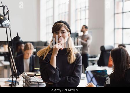 Ritratto di donna d'affari sorridente con mano sul mento in ufficio Foto Stock