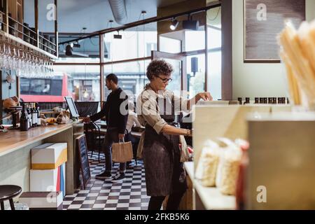 Donna proprietario del negozio che lavora in deli store con i clienti in sfondo Foto Stock