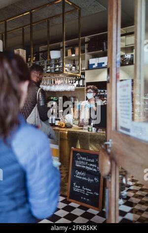 I clienti mantengono la distanza sociale durante la raccolta degli ordini dal negozio di gastronomia Durante COVID-19 Foto Stock