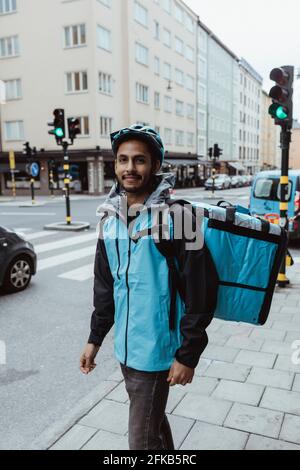 Ritratto di sorridente delivery man in piedi sul marciapiede in città Foto Stock