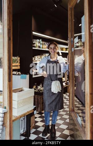 Ritratto di giovane donna sorridente proprietario in piedi da porta di negozio di delicatessen Foto Stock