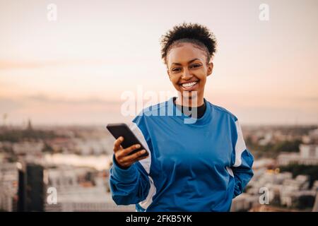 Ritratto di una donna sportiva sorridente che tiene lo smartphone durante il tramonto Foto Stock