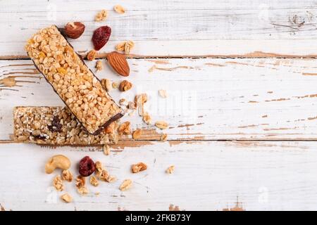Un'unica barra energetica a base di granola con noci miste sparse, cereali e frutta secca, sfondo di tavola in legno bianco grunged. sano nutritivo vegan fi Foto Stock