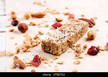 Un'unica barra energetica a base di granola con noci miste sparse, cereali e frutta secca, sfondo di tavola in legno bianco grunged. sano nutritivo vegan fi Foto Stock