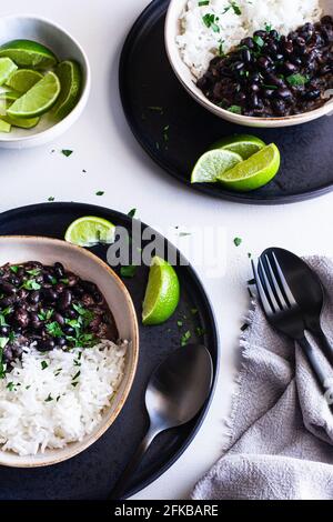 Due ciotole di fagioli neri cubani servite con riso e spicchi di lime. Foto Stock