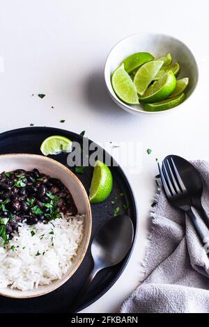 Ciotola di fagioli neri cubani servita con riso e spicchi di lime. Foto Stock