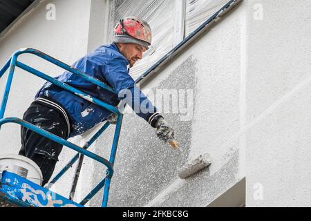 Bielorussia, Minsk - 28 maggio 2020: Lavoratore su una piattaforma di sollevamento che dipinge una nuova facciata di una casa in costruzione in un cantiere. Foto Stock