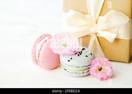 Dolci francesi al deserto al mirtillo e alla fragola, scatola presente avvolta in carta marrone artigianale, legata con arco giallo seta, fioritura primaverile. Foto Stock