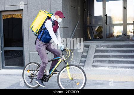 Corriere giovane che consegna il cibo con uno zaino termale giallo, in bicicletta in città. Concetto di servizio di consegna di cibo Foto Stock