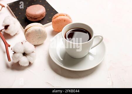 Composizione elegante, macaron al cioccolato assortiti francesi, tazza da caffè, taccuino, bol di cotone, tavolo con intonaco bianco. Buon compleanno mothe Foto Stock