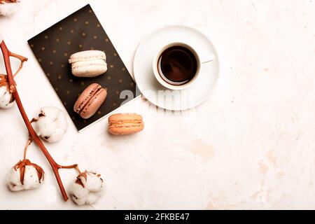 Composizione elegante, macaron al cioccolato assortiti francesi, tazza da caffè, taccuino, bol di cotone, tavolo con intonaco bianco. Buon compleanno mothe Foto Stock