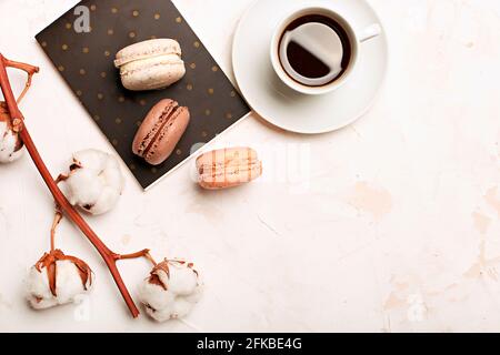 Composizione elegante, macaron al cioccolato assortiti francesi, tazza da caffè, taccuino, bol di cotone, tavolo con intonaco bianco. Buon compleanno mothe Foto Stock