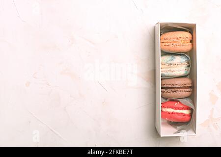 Dolci alla amarina francese, gusti e colori diversi. Scatola di macaron su fondo bianco stucco intonaco tessitura tavolo. Compleanno San Valentino donne giorno spri Foto Stock