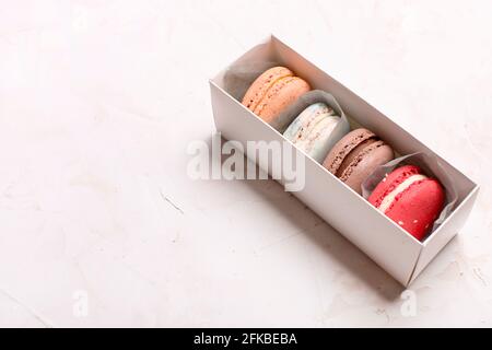 Dolci alla amarina francese, gusti e colori diversi. Scatola di macaron su fondo bianco stucco intonaco tessitura tavolo. Compleanno San Valentino donne giorno spri Foto Stock