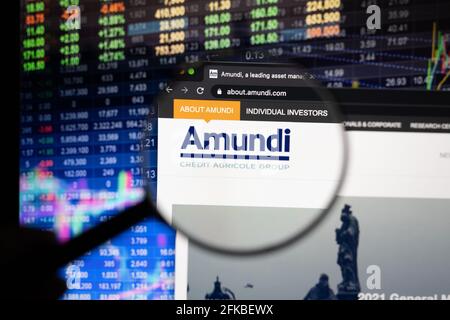 Amundi logo aziendale su un sito web con sviluppi sfocati del mercato azionario sullo sfondo, visto su uno schermo del computer attraverso una lente di ingrandimento Foto Stock