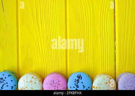 Dolci alla amarina francese, gusti e colori diversi. Macaron su sfondo giallo tavola di legno tessitura. Compleanno San Valentino presente. Copia testo sp Foto Stock