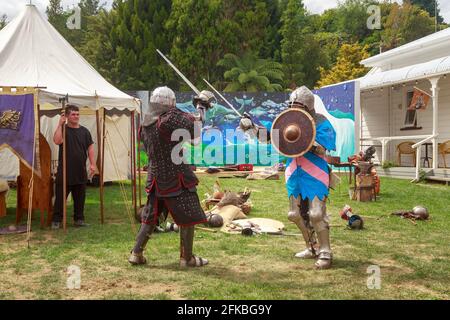 I reenattori di cavaliere vestiti in catena e armatura di piastra, duellando con spade in una fiera medievale Foto Stock