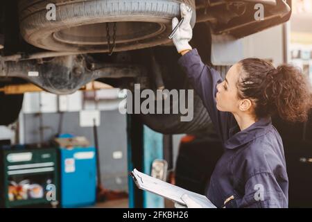 Donna Garage operaio manutenzione lista di controllo presso il centro di servizio di automobile, femmina in auto meccanico tecnico di servizio di lavoro di controllo e riparazione del cliente Foto Stock