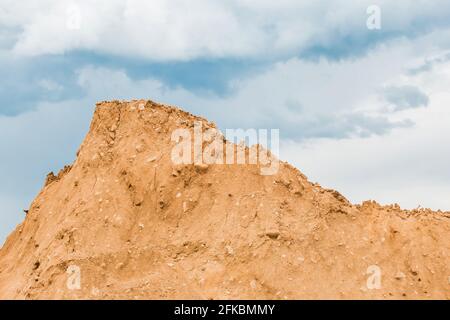 Grande mucchio di materiale naturale di sabbia in un luogo di costruzione contro un cielo blu. Foto Stock