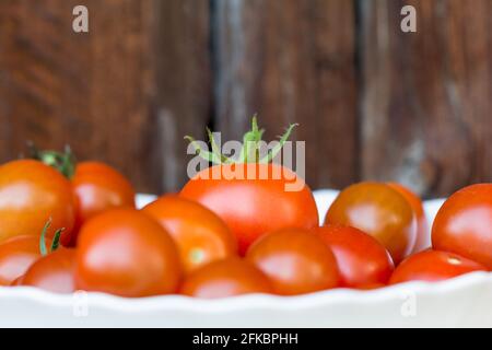 Raccogliere un mazzo di gustosi pomodori rossi in una ciotola bianca. Deliziose verdure fresche e succose provenienti dall'agricoltura. Natura biologica solanum pomodoro fo Foto Stock