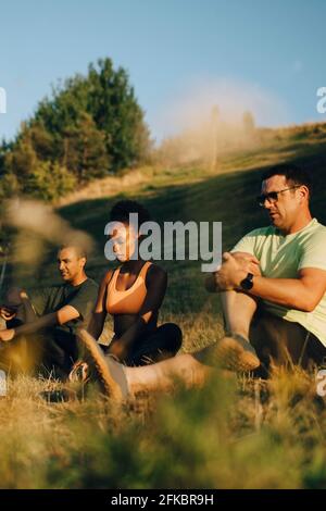 Atlete maschili e femminili meditating mentre sedendo sull'erba dentro parcheggia durante la giornata di sole Foto Stock