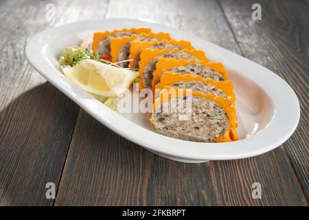 Pasta di carne mista a fette con brillante cima arancione servita su piatto di ceramica bianca con limone e germogli freschi. Primo piano di gustoso piatto su tavola di legno in r Foto Stock