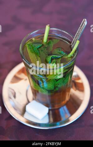 Bicchiere alto con tè alla menta berbero dolce e piatto di metallo con un cubo di zucchero bianco, autentica bevanda gourmet con un fresco aroma minty e dolce Foto Stock