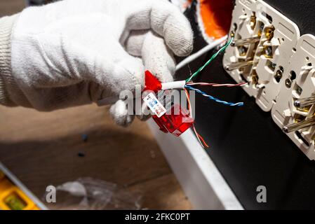 Un elettricista in guanti bianchi sta installando un cavo di rete per il modulo RJ45 alla presa del computer nella stanza. Foto Stock