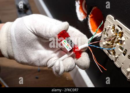 Un elettricista in guanti bianchi sta installando un cavo di rete per il modulo RJ45 alla presa del computer nella stanza. Foto Stock