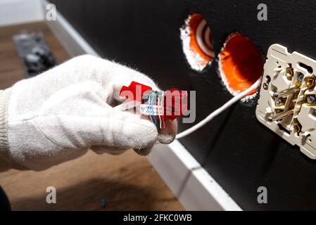 Un elettricista in guanti bianchi sta installando un cavo di rete per il modulo RJ45 alla presa del computer nella stanza. Foto Stock