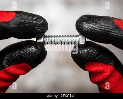 Persone che indossano guanti di protezione che trattengono il bullone e il dado contro il metallo sfondo Foto Stock