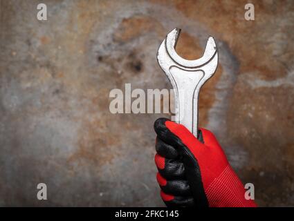 Persona che indossa un guanto di protezione che tiene la chiave grande contro il metallo arrugginito sfondo Foto Stock