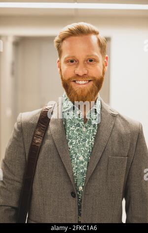 Uomo d'affari bearded sorridente in corridoio all'ufficio Foto Stock