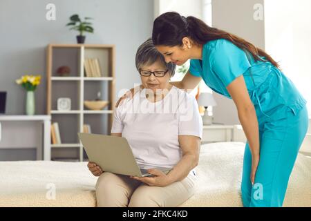 Infermiera donna che aiuta la paziente anziana della signora con il laptop a casa ritratto stile di vita Foto Stock