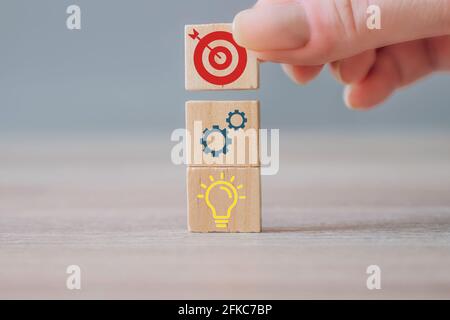 Strategia aziendale, piano d'azione, concetto di gestione. Uomo d'affari mano mettendo legno cubo blocco con l'icona di destinazione in cima ad altri cubi con il commercio Foto Stock
