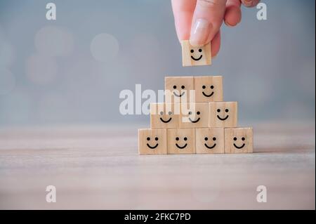 Miglior eccellente valutazione dei servizi aziendali, concetto di esperienza del cliente. Mano mettendo blocco cubo di legno con felice faccia smiley icona. Sondaggio sulla soddisfazione Foto Stock