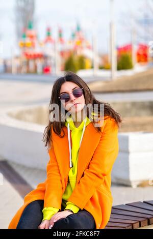 Elegante bella giovane donna vivido vestito si siede sullo sfondo di colori luminosi della strada della città. Stile di vita ritratto millenario Hipster Girl Foto Stock