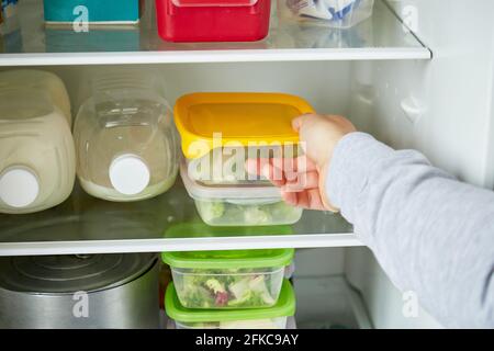 Il giovane mette i contenitori nel frigorifero. Il concetto di preparare e conservare cibo domestico o ristorante per un lungo periodo. Foto di alta qualità Foto Stock