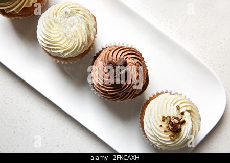 Vista dall'alto di un vassoio bianco con una varietà di gusti cupcake su sfondo bianco in marmo Foto Stock