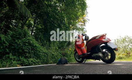 La moto rossa sulla strada forestale viaggio. Uno scooter, vicino a palme tropicali. Asia Thailandia giro turistico. Moto singola, noleggio. Foto Stock