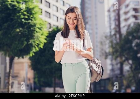 Ritratto fotografico di una studentessa con zaino digitando sms utilizzando telefono cellulare a piedi lungo la strada della città al college Foto Stock