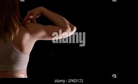 Donna torna in abbigliamento sportivo durante l'allenamento in posa su uno sfondo nero isolato senza volto. L'immagine mostra i muscoli femminili e un corpo sano e bello Foto Stock