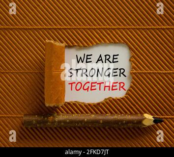 Simbolo di Unione più forte. Parole Siamo più forti insieme che appaiono dietro la carta marrone strappata. Matita di legno. Business, motivazionale e siamo più forti Foto Stock
