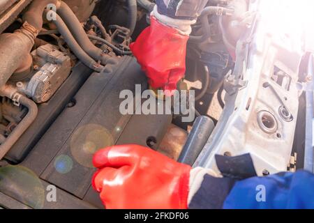 Un uomo in guanti di gomma rossa cambia l'olio in un motore di automobile. Riparazione auto con cofano sollevato Foto Stock