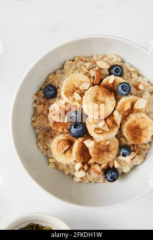 Ciotola di porridge ricoperta di banana, mirtilli, mandorle e cannella Foto Stock