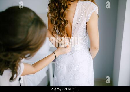 La bridesmaid aiuta la sposa a buttare su l'abito durante la preparazione per la cerimonia nuziale, vista posteriore Foto Stock