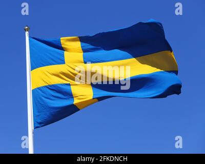 Vista ravvicinata della bandiera svedese che si volta contro un cielo blu chiaro. Foto Stock